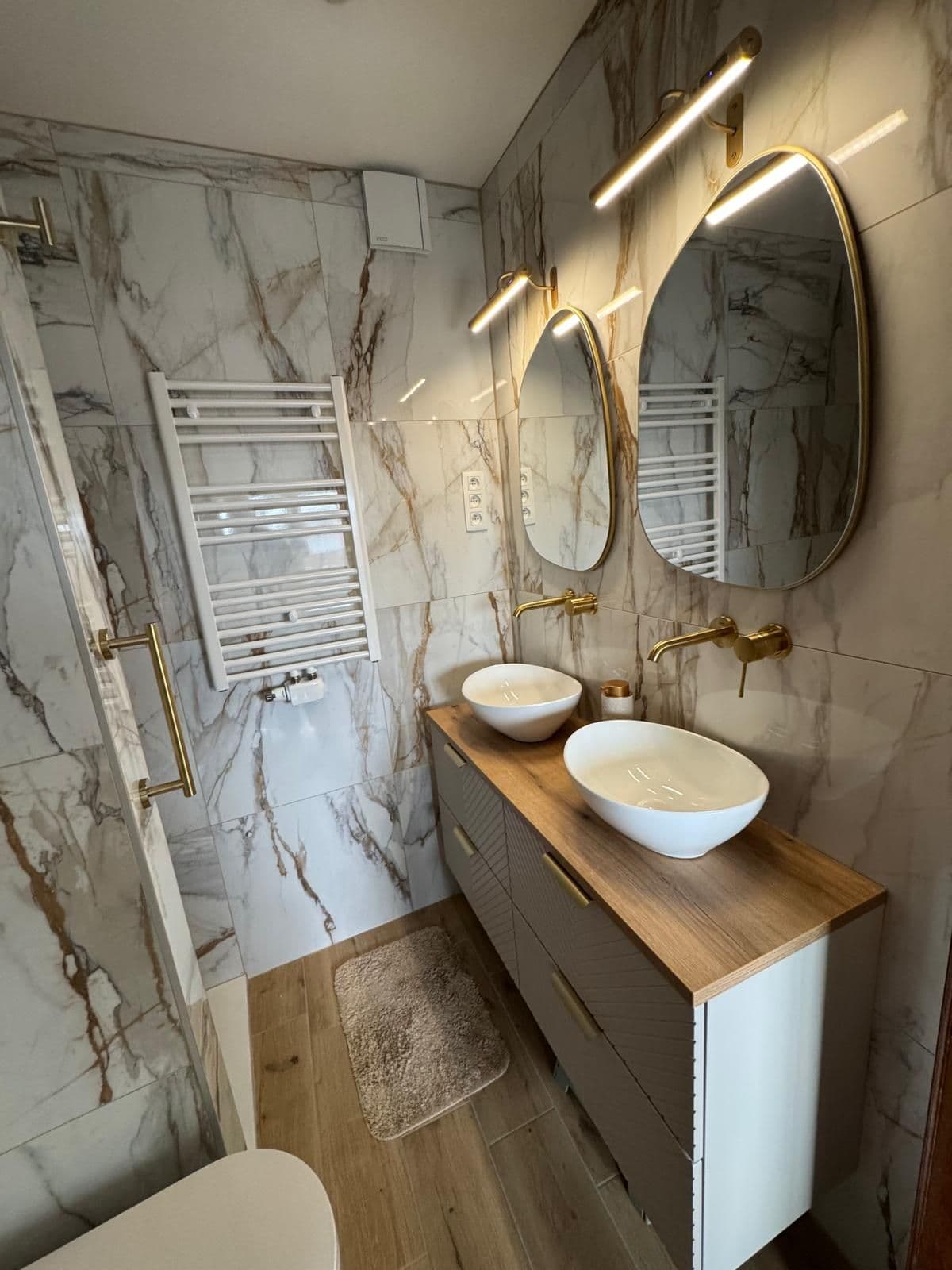 Double vasque en marbre veiné avec miroirs ovales dorés et mur en pierre verte, après rénovation